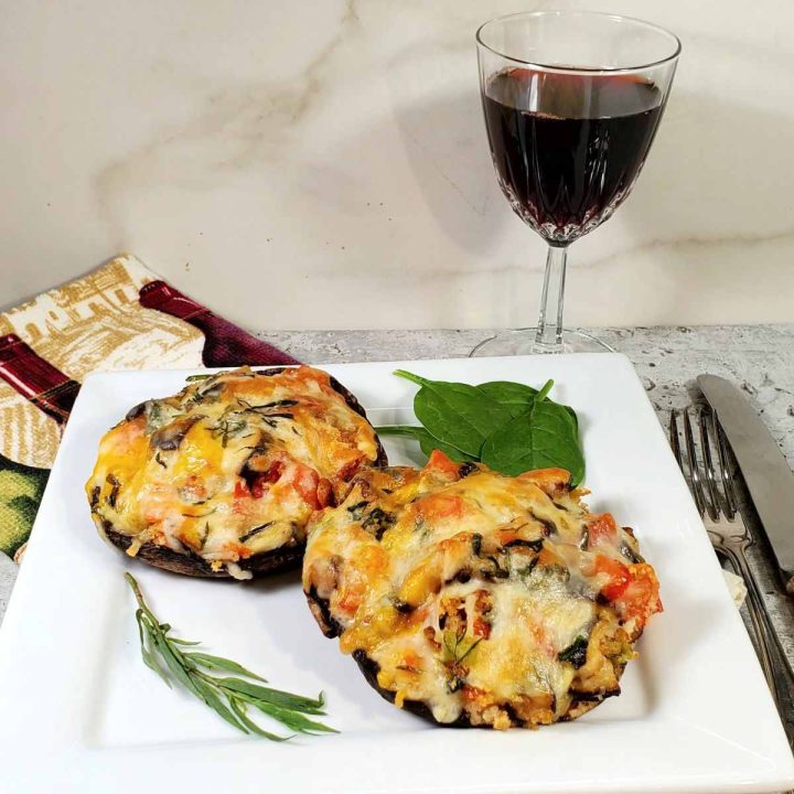 Two stuffed portobello mushrooms on a white plate with a glass of wine and cutlery.