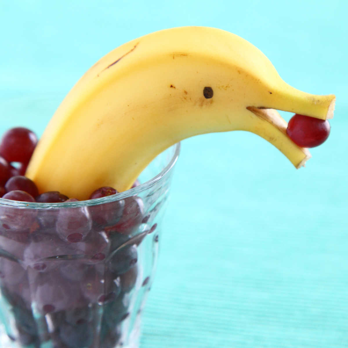 Half a banana sitting in a glass of grapes, shaped like a dolphin - a fun banana food art creation.