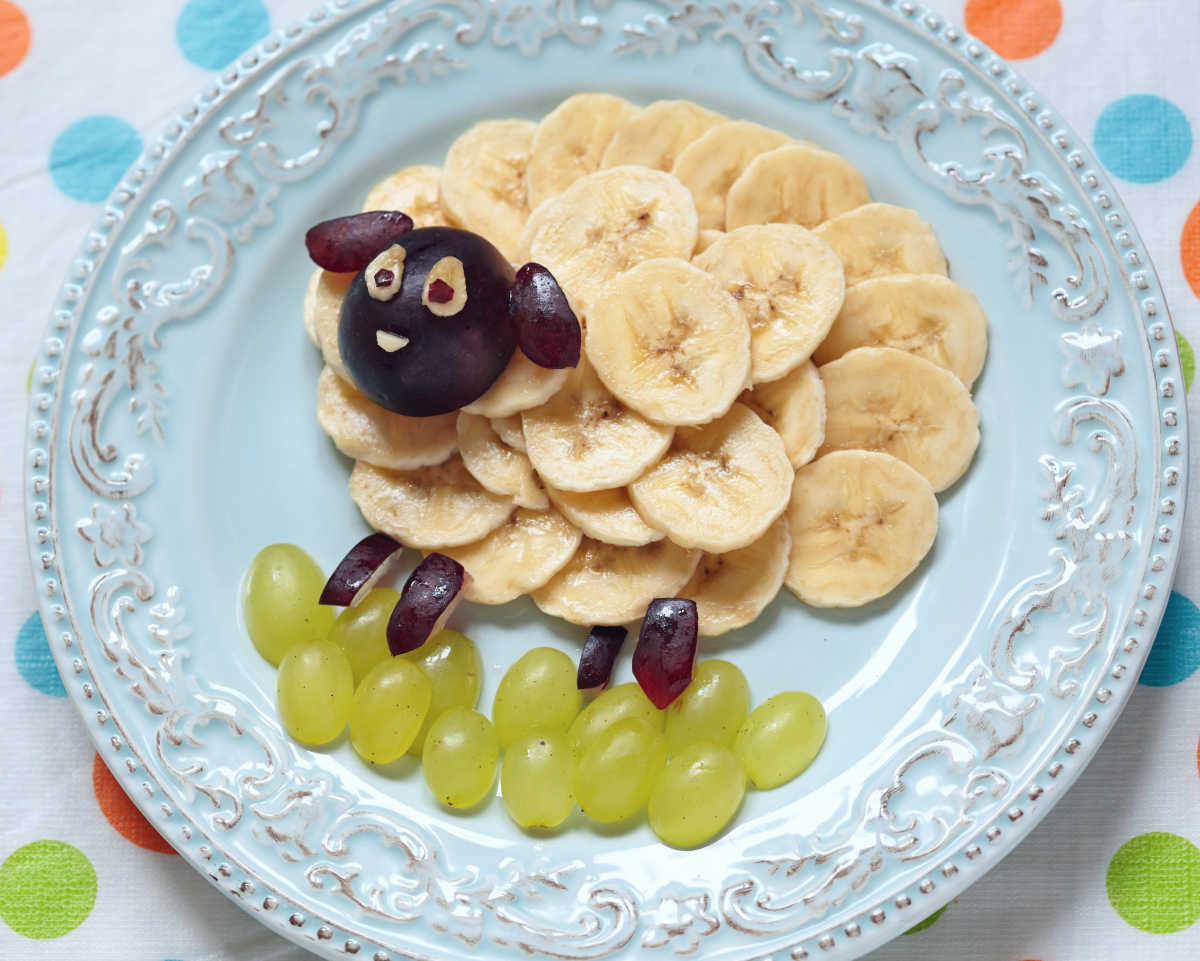 A sheep on a blue plate made from grapes and bananas.