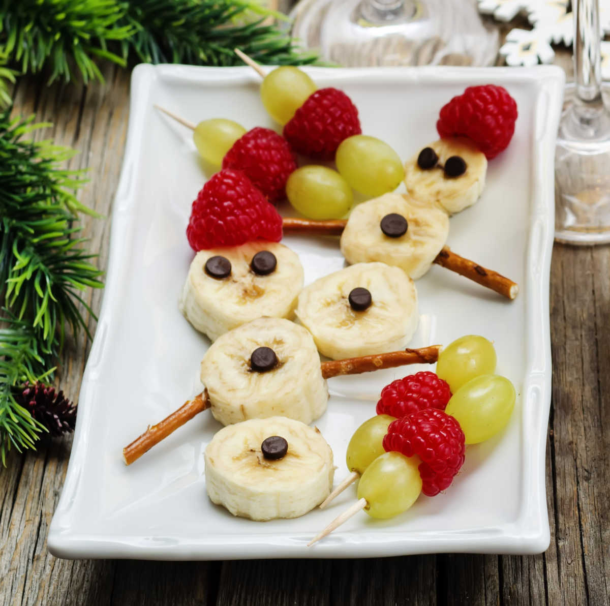 Sbowmen made with bananas, pretzels , grapes, and strawberries - A holiday banana food art project.