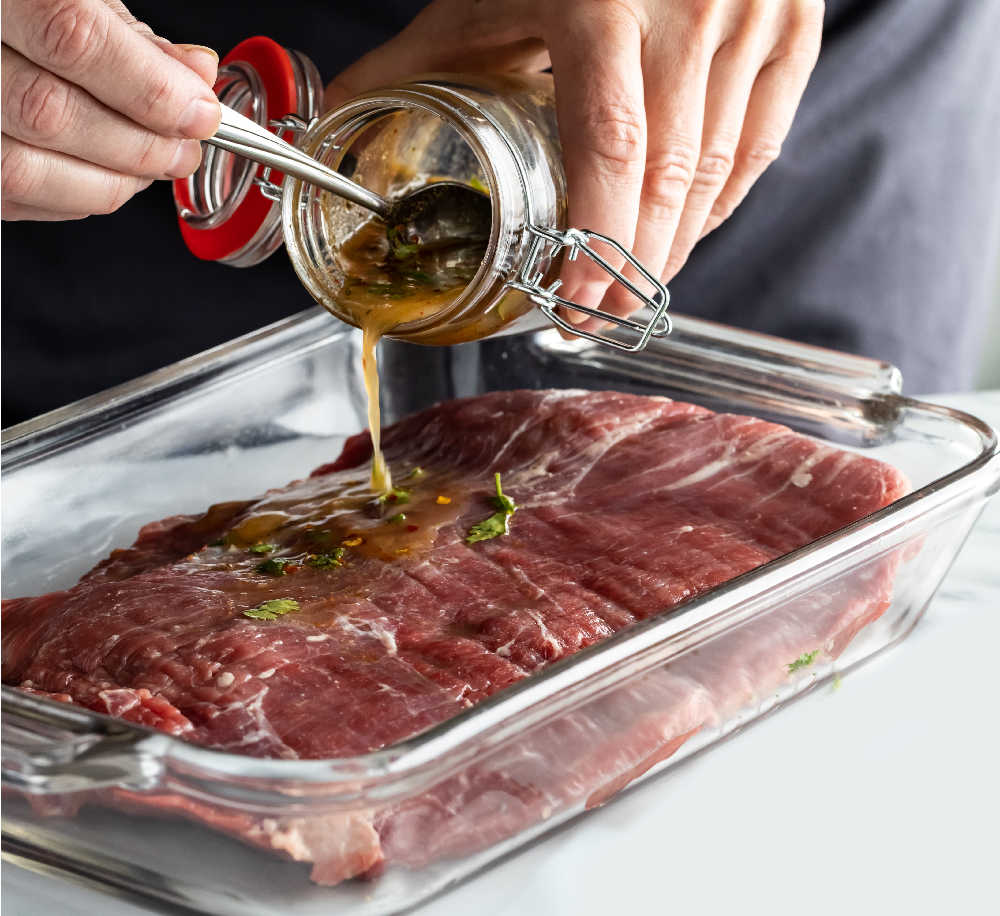 Hands pouring marinade on steaks.