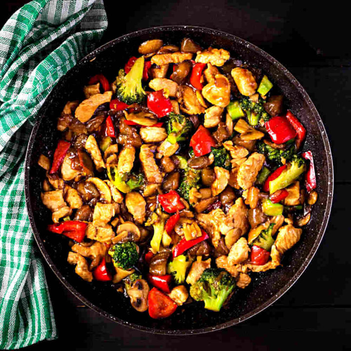 Stir fry in a bowl on a black background with checked green towel.