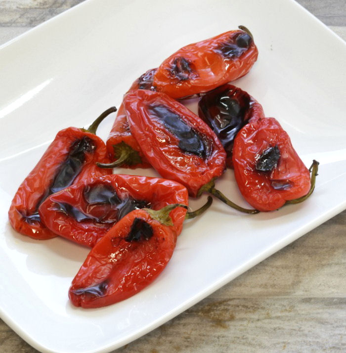 Roasted red peppers with charred spots on a white plate.