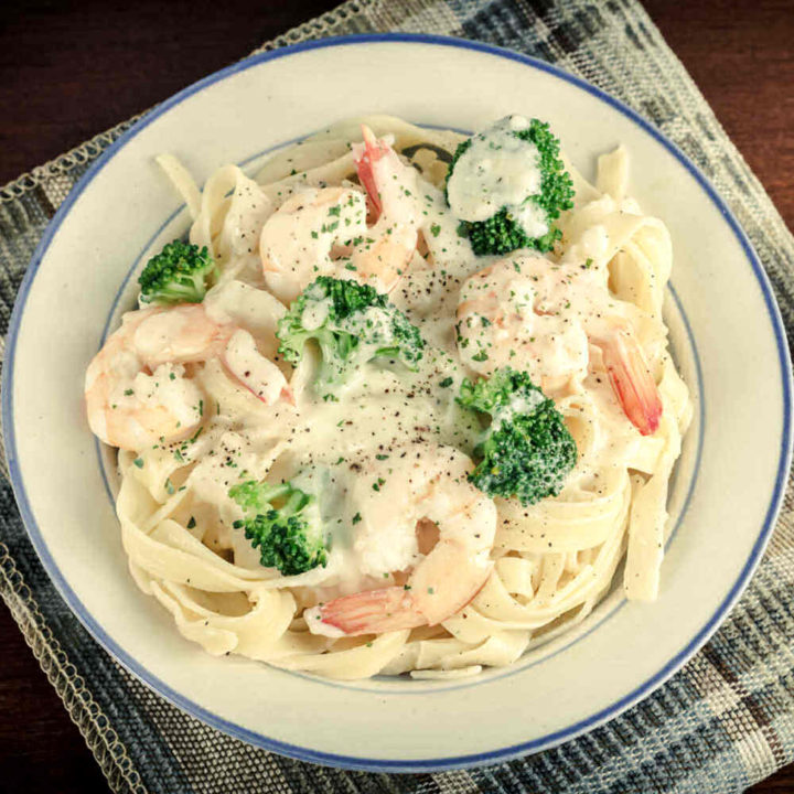 Shrimp pasta with broccoli in a blue and white bowl.