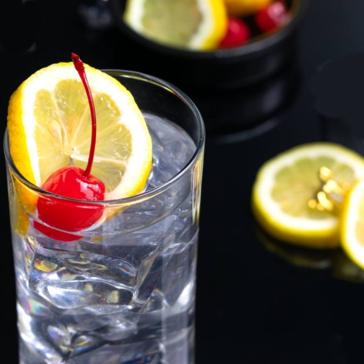 Tom Collins in a glass with ice, lemon and a cherry.
