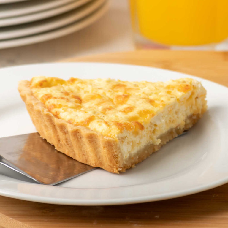 Cheese quiche on a white plate with orange juice.