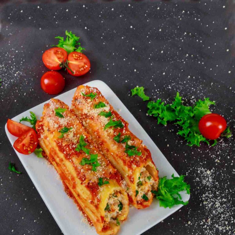 Homemade manicotti recipe on a white plate with tomatoes, salt and herbs.