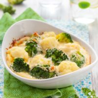 Broccoli and cauliflower with cheddar cheese in a white dish with a green napkin.