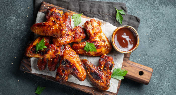 Sticky chicken wings on a paper coated wooden board with fresh parsley and sauce.