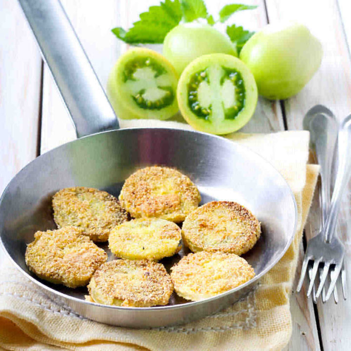 Green tomatoes and fried green tomatoes in a frying pan with a fork.