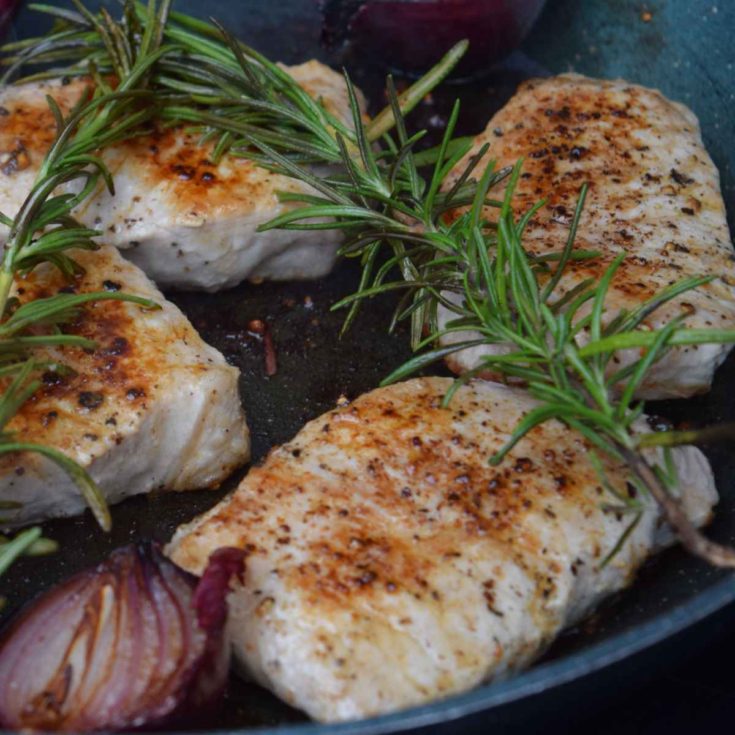 Grilled pork chops on a plate with fresh rosemary.