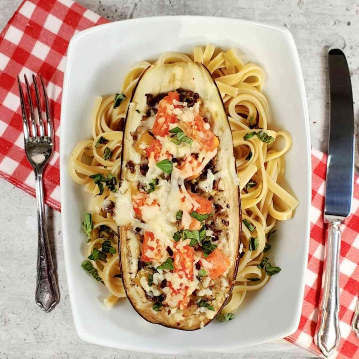 Beef stuffed eggplant on a bed of spaghetti in a white bowl with a red napkin.