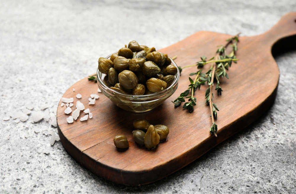 Bowl of capers with coarse salt and fresh thyme on a cutting board.
