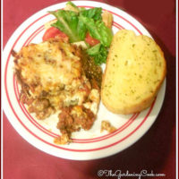 Eggplant lasagne and garlic bread with salad on a white and red plate.