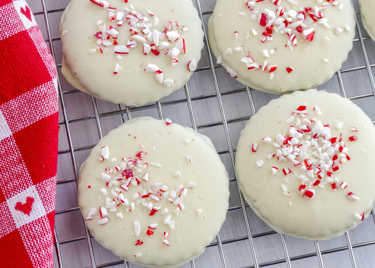 White chocolate cookies sprinkled with crushed peppermints on a wire rack next to a red checked tea towel.