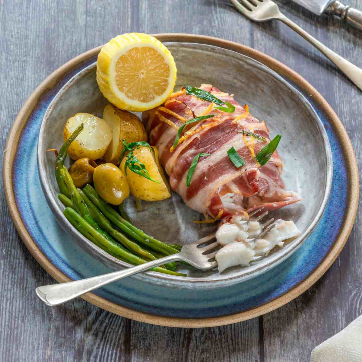 Bacon wrapped haddock with beans, potatoes and lemon slices.
