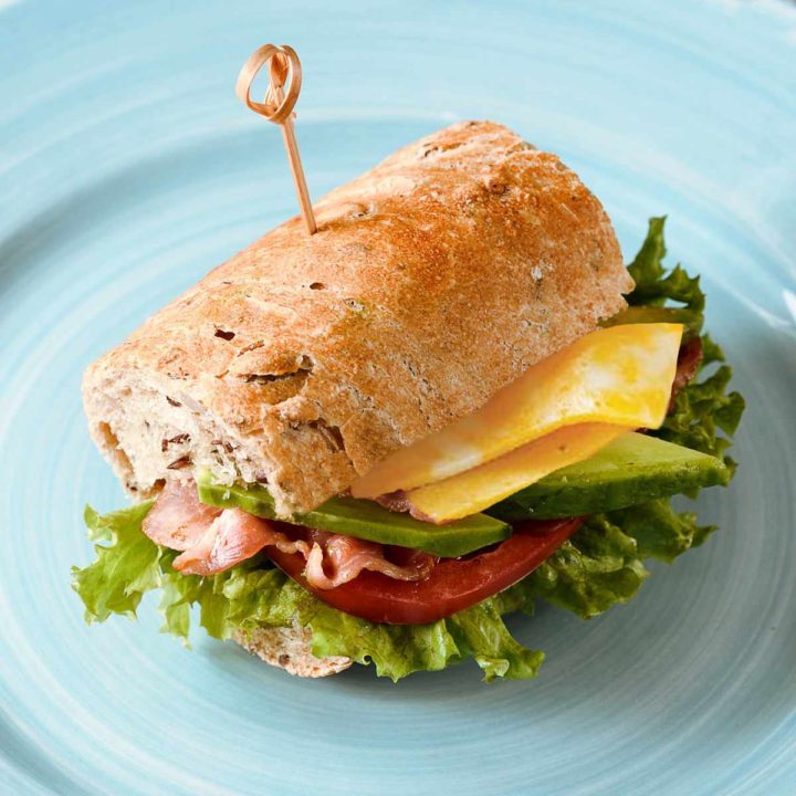 Blt sandwich with avocado and cheese on a blue plate.