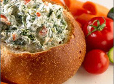 Spinach dip in a bread bowl with tomatoes.