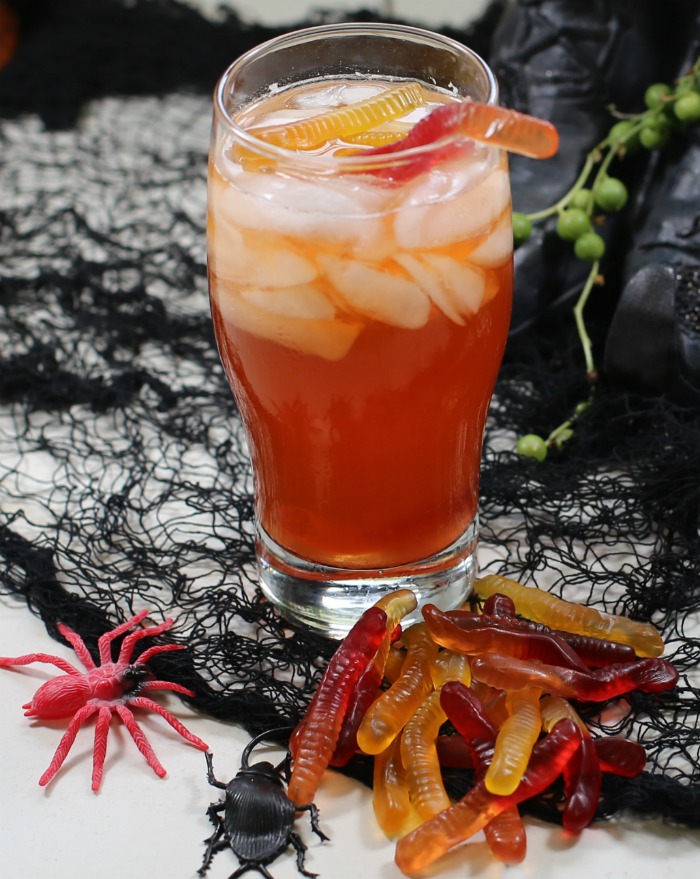 Halloween cocktail garnishes - gummy worms draped over the edge of a glass with black spider web.