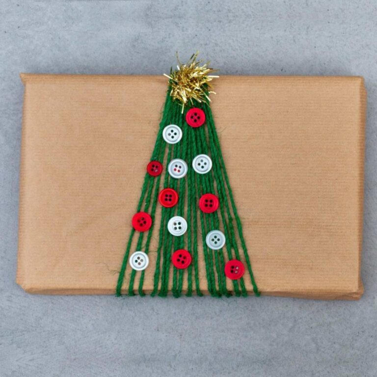 A creative holiday gift wrapping idea showing a rectangular package wrapped in brown paper, with green string wrapped around it to resemble a tree, buttons glued down to stand in for ornaments and a small piece of garland at the top to resemble a star tree topper.