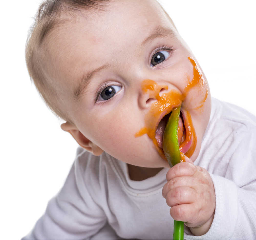 Baby with spoon and food on face.
