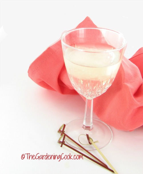 Frozen wine cubes in a glass of wine with cocktail sticks and a peach colored napkin.