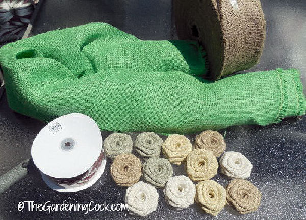 Supplies for making a DIY burlap wreath - green burlap, wire edged ribbon and rows of burlap rose flowers.