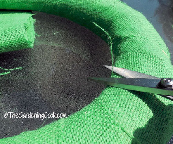 A pair of scissors trimming frayed fabric on a burlap wreath.