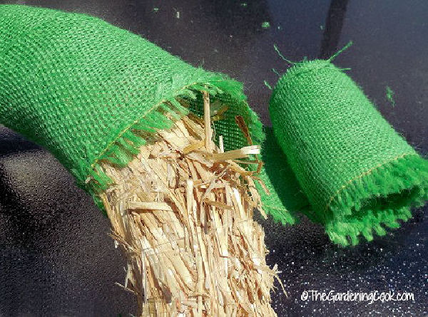 A straw wreath covered in green burlap next to a roll of green burlap fabric.