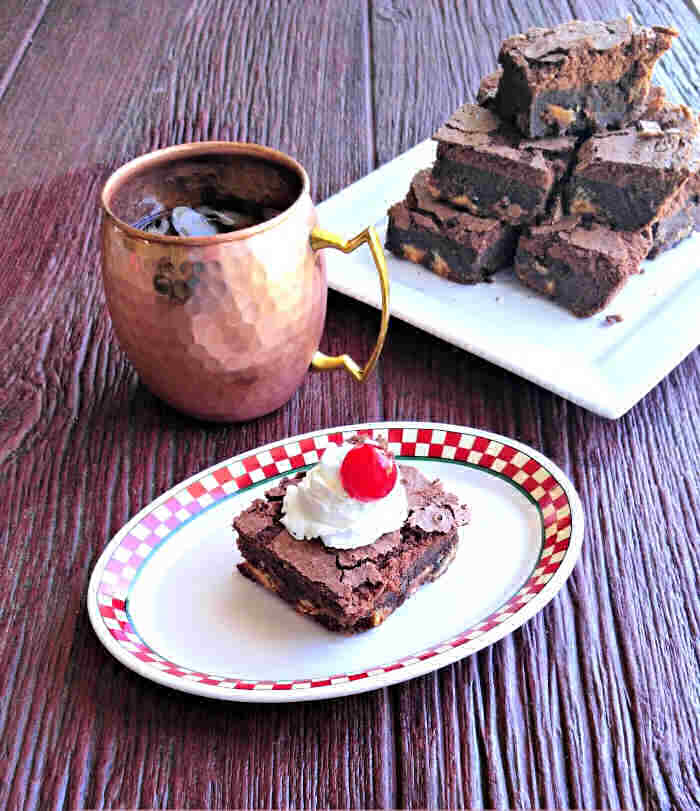 Brownie on a checked plate with a plate of brownies and a copper mug.