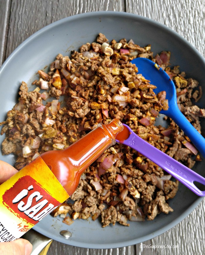 Ground beef in a pan with spoons and hot sauce.