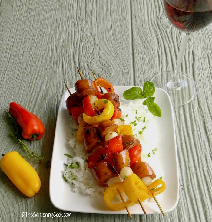 Cajun style Andouille sausage kebabs on a plate with wine and peppers.