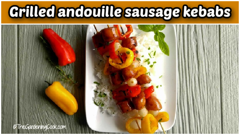 Grilled andouille sausage kebabs on a flowered plate with peppers beside it.