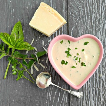 Heat shaped bowl and spoon filled with parmesan dressing recipe and basil and cheese.
