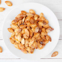 Roasted pumpkin seeds on a white plate.