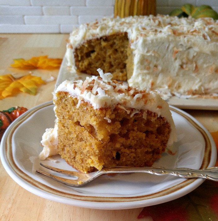 Slice of pumpkin spice cake with a toasted coconut frosting on a white plate with a fork.
