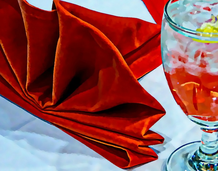 Folded red velvet napkin and drink with red beverage in it.