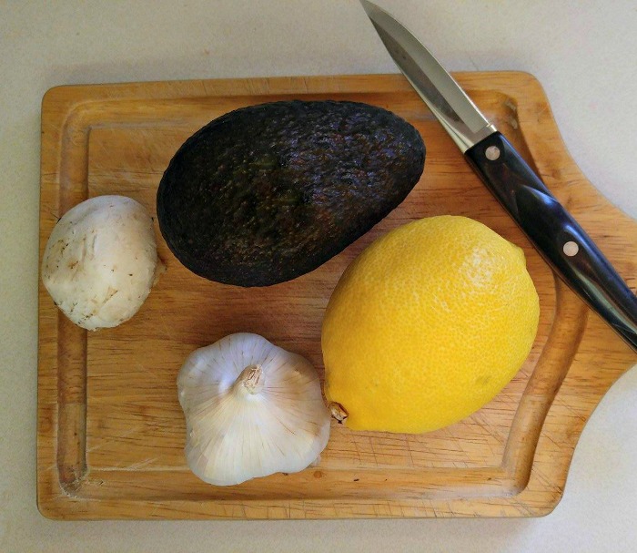 Avocado, lemon, garlic and mushroom on a cutting board with a knife.