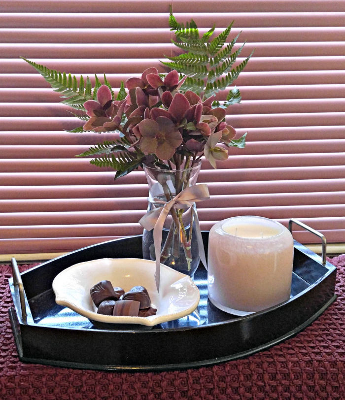 Pink Alassa candle on a tray with chocolates and Monrovia hellaborus flowers