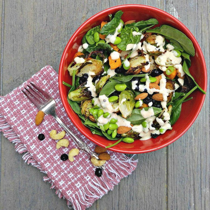 Tasty roast vegetable salad with a pink napkin, fork, blueberries and nuts.