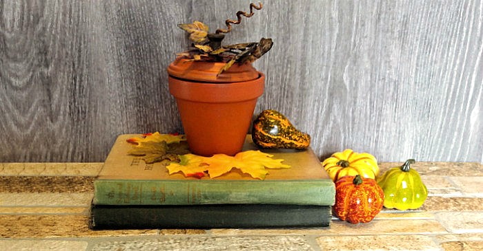 clay pot pumpkin A clay pot made into a pumpkin candy dish sitting on top of old books with fall leaves and mini pumpkins.