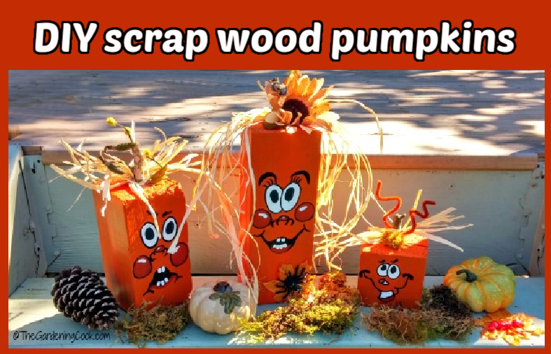 Three blocks of reclaimed wood painted orange with hand painted faces, flowers and straw to decorate, sitting next to pinecones, leaves and baby pumpkins.