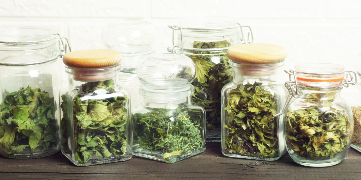 Dried herbs in glass bottles on a wooden counter.