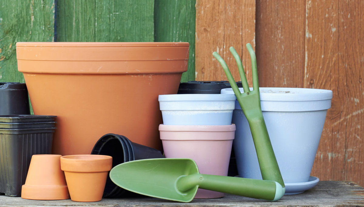 A group of clean clay pots and poastic pots with garden tools, stored in a shed.