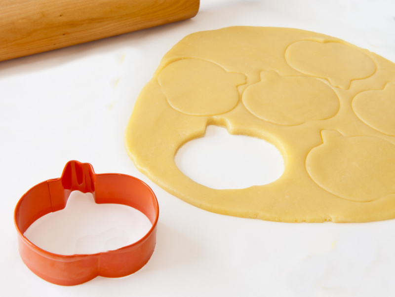 Orange cookie cutter next to some chilled dough and rolling pin.