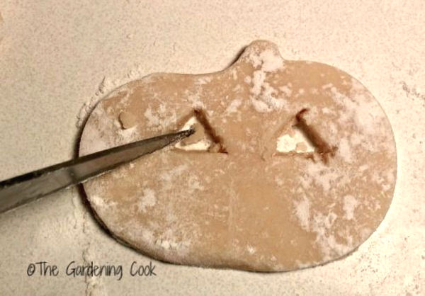 Chilled dough on a floured countertop with a knife cutting eyes in the dough.