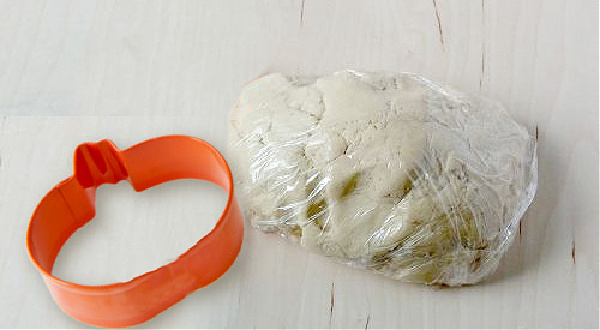 Orange cookie cutter sitting next to some cookie dough wrapped in plastic.
