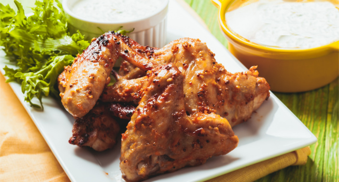 Honey garlic chicken wings on a plate with celery and bowls or ranch dressing and tzatziki sauce.