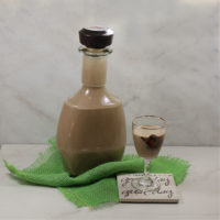 Home Made Baileys in a bottle and glass with a green piece of fabric.
