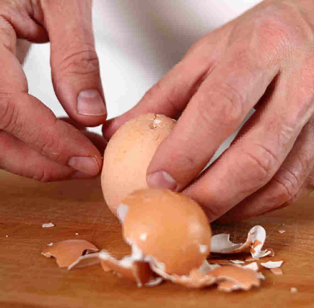 Hands tapping a hard boiled egg to crack the shell.